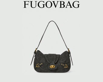 May include: A dark gray shoulder bag with a flap closure and a long strap. The bag features gold-colored hardware, including a clasp and decorative rings. The word "FUGOVBAG" is printed at the top.