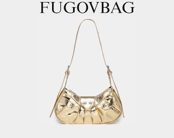May include: A gold-colored shoulder bag with a bow-shaped design. The bag has a textured, metallic finish and a thin, adjustable strap. The word "FUGOVBAG" is printed at the top.