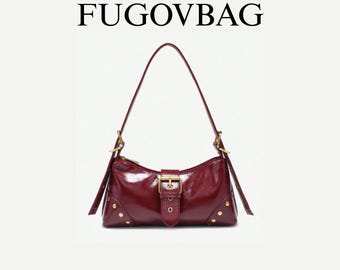 May include: A burgundy shoulder bag with a glossy finish. The bag has a buckle closure, gold-coloured hardware, and small gold studs. It features a long strap and the text "FUGOVBAG" is at the top.