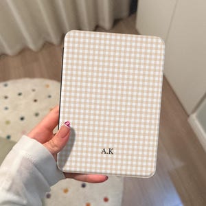 May include: A rectangular phone case with a beige and white gingham pattern. The initials "A.K" are printed in the center. The case is held in a hand.