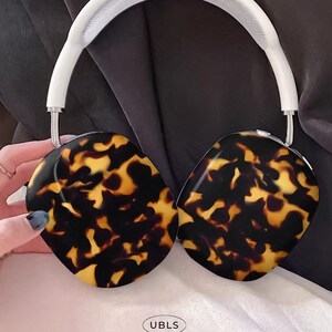 Może przedstawiać: Słuchawki nauszne z białym pałąkiem i nausznikami z wzorem w kolorze żółto-brązowym. Słuchawki mają elegancki, nowoczesny design, a widoczny jest tekst "UBLS".