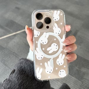 May include: Clear phone case with a white bunny and star pattern. The case has a clear border and a white circular design with bunny faces. The case has the text "UBLS" at the bottom.