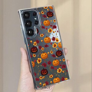 May include: Clear phone case with a Halloween-themed pattern. The design features orange jack-o'-lanterns and yellow and red flowers on a gray background. The case has a clear border and a camera cutout.