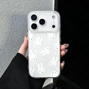 May include: Clear phone case with a white bunny and star pattern. The case has a transparent border and covers the back and sides of the phone. The case has a camera cutout and the text "UBLS" at the bottom.