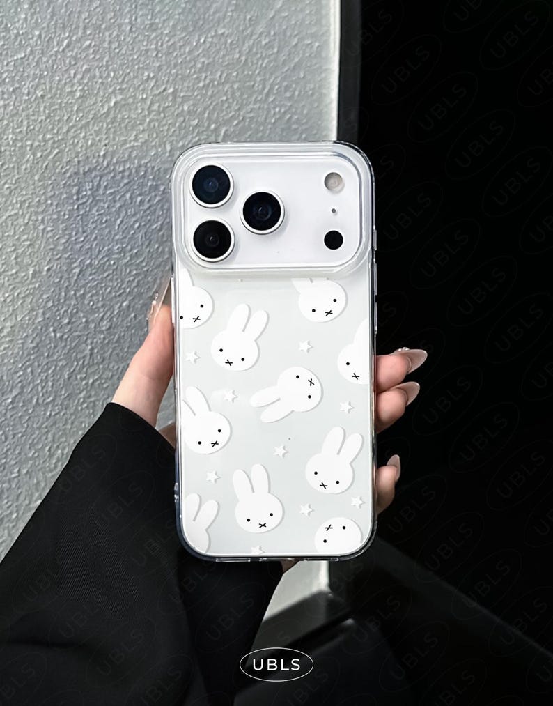 May include: Clear phone case with a white bunny and star pattern. The case has a transparent border and covers the back and sides of the phone. The case has a camera cutout and the text "UBLS" at the bottom.