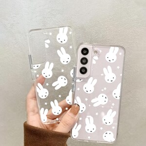 May include: Clear phone case with a white bunny and star pattern. The case is shown with a phone inside, and a separate empty case. The phone case has a camera cutout and button cutouts.