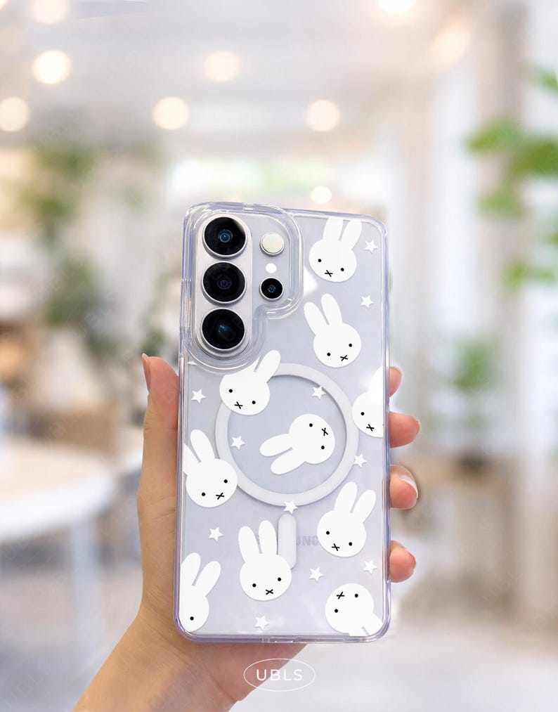 May include: Clear phone case with a white bunny and star pattern. The case has a camera cutout and a circular design in the center. The bottom of the case has the text "UBLS".