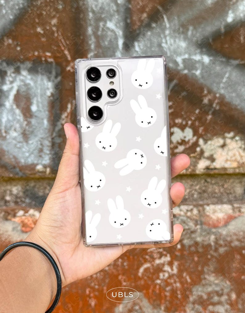 May include: Clear phone case with a repeating pattern of white bunny faces and stars on a light gray background. The case has a clear border and a camera cutout.