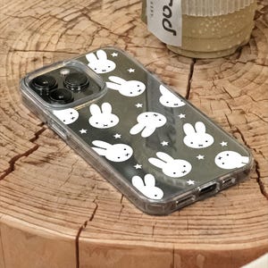 May include: Clear phone case with a black background featuring a pattern of white bunny faces and stars. The case has a transparent border and covers the phone's camera and buttons. The brand name "UBLS" is visible on the bottom.
