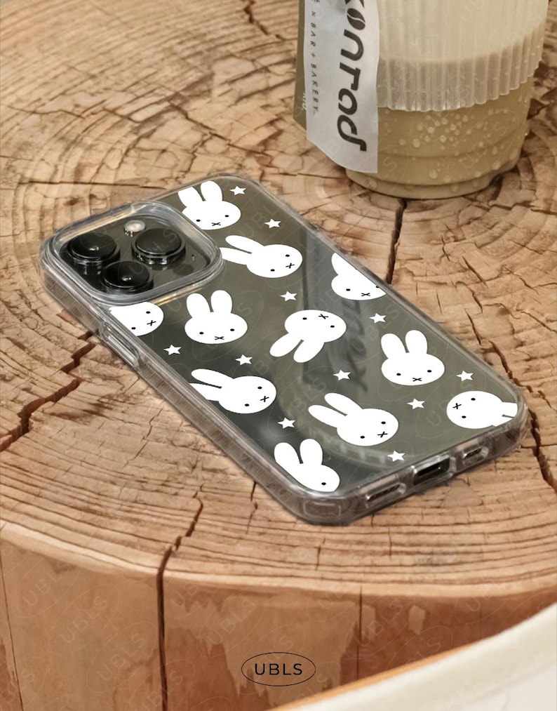 May include: Clear phone case with a black background featuring a pattern of white bunny faces and stars. The case has a transparent border and covers the phone's camera and buttons. The brand name "UBLS" is visible on the bottom.