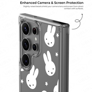 May include: Clear phone case with a gray background and white bunny and star pattern. The case has a protective design with slightly raised bezels to shield the camera lens and screen from contact with surfaces. Text on the case reads: Enhanced Camera & Screen Protection.
