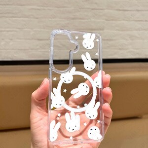 May include: Clear phone case featuring a repeating pattern of white cartoon bunny faces and stars. The case has a cutout for the camera and a circular design of bunnies. The text "UBLS" is printed at the bottom.