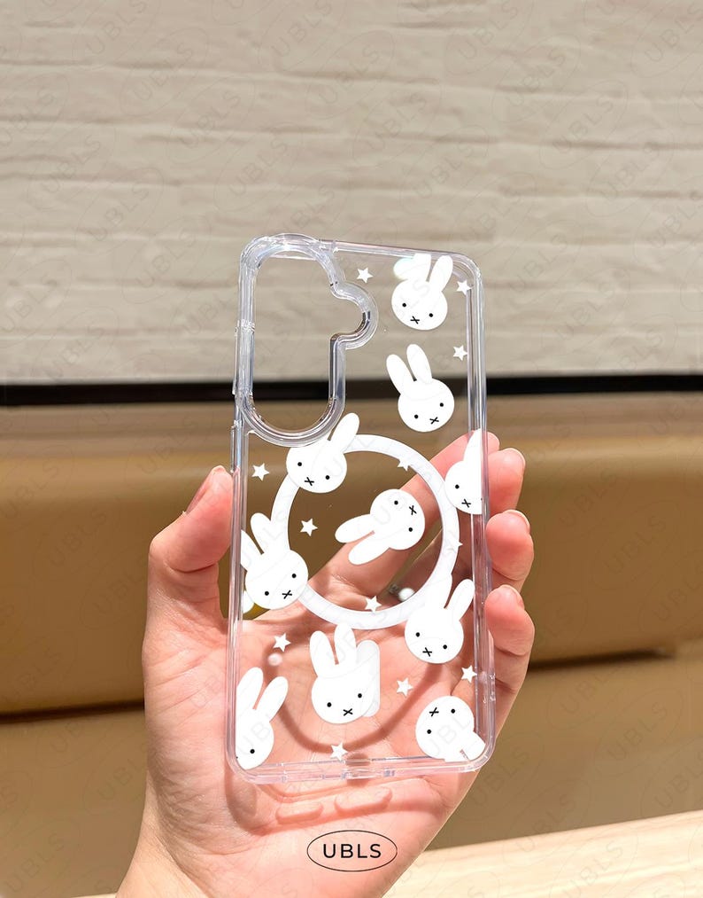 May include: Clear phone case featuring a repeating pattern of white cartoon bunny faces and stars. The case has a cutout for the camera and a circular design of bunnies. The text "UBLS" is printed at the bottom.