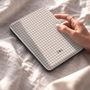 May include: A tablet case with a beige and white gingham design. The case has a black border and the initials "F♡A" in black. The case is on a white, textured surface.