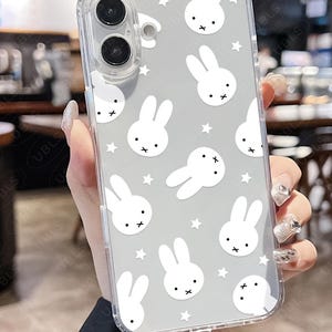 May include: Clear phone case with a gray background featuring white bunny illustrations and small white stars. The case has a transparent border and covers the phone's camera and buttons.
