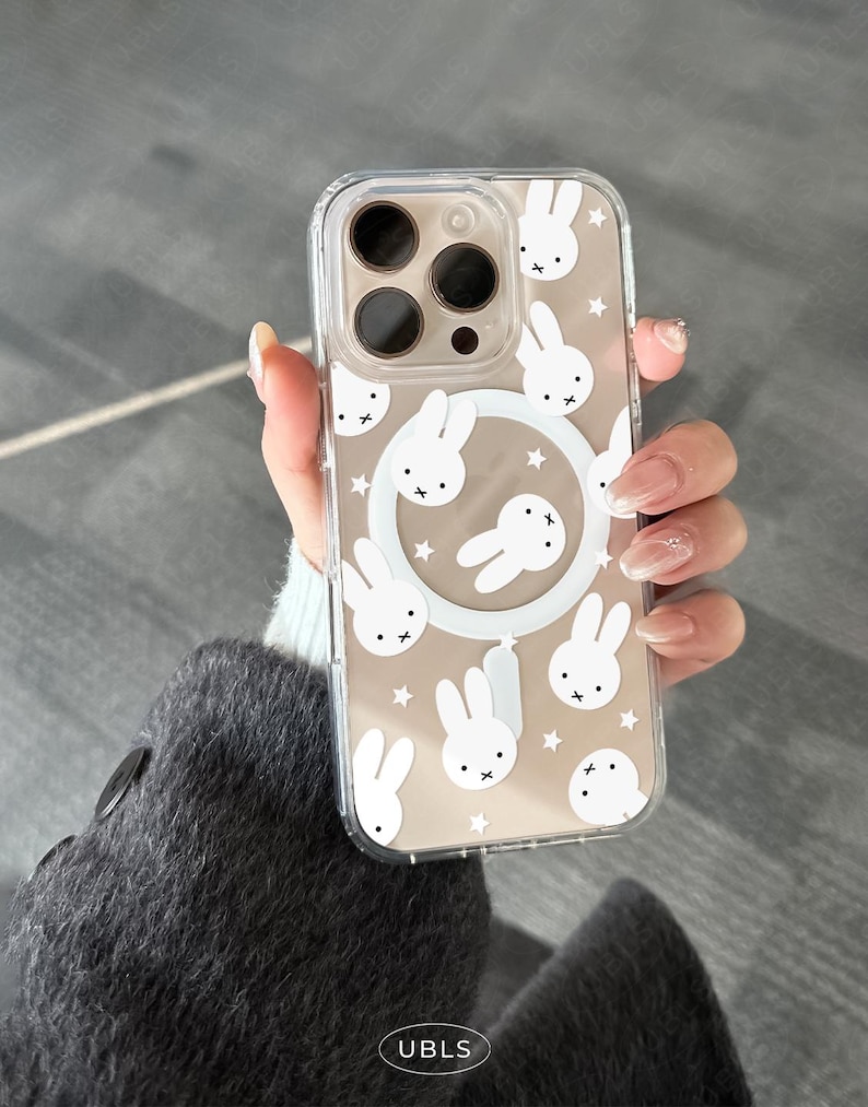 May include: Clear phone case with a white bunny and star pattern. The case has a clear border and a white circular design with bunny faces. The case has the text "UBLS" at the bottom.