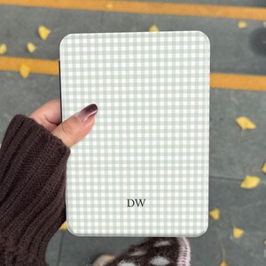 May include: A rectangular phone case featuring a light green and white gingham design. The initials "DW" are printed on the front. The case is held by a person wearing a brown sweater.