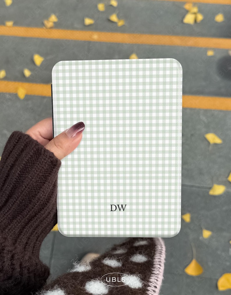 May include: A rectangular phone case featuring a light green and white gingham design. The initials "DW" are printed on the front. The case is held by a person wearing a brown sweater.