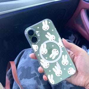 May include: Clear phone case with a green tint, featuring a pattern of white bunny faces and stars. The case has a circular white design in the center and two camera cutouts. The text "UBLS" is visible on the bottom.