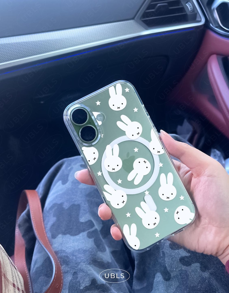 May include: Clear phone case with a green tint, featuring a pattern of white bunny faces and stars. The case has a circular white design in the center and two camera cutouts. The text "UBLS" is visible on the bottom.
