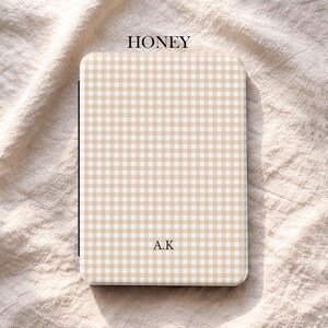 May include: A rectangular case featuring a honey-coloured gingham pattern. The text "HONEY" is at the top, and "A.K" is printed below. The bottom of the case has the text "UBLS".