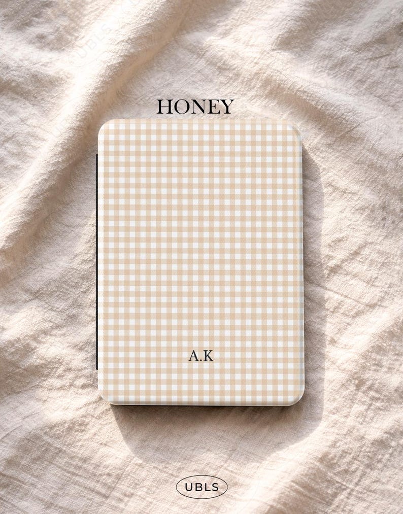 May include: A rectangular case featuring a honey-coloured gingham pattern. The text "HONEY" is at the top, and "A.K" is printed below. The bottom of the case has the text "UBLS".