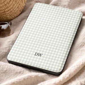 May include: A phone case featuring a light green and white gingham design. The initials "DW" are printed on the case. The case is set on a beige fabric, with a straw bag and sunglasses visible in the background.