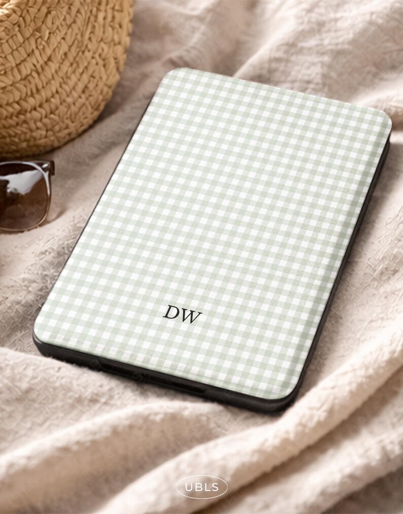 May include: A phone case featuring a light green and white gingham design. The initials "DW" are printed on the case. The case is set on a beige fabric, with a straw bag and sunglasses visible in the background.