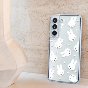 May include: Clear phone case featuring a repeating pattern of white cartoon bunny faces and stars. The case has a transparent border and is designed to fit a smartphone. The UBLS logo is visible at the bottom.