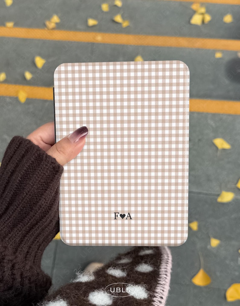 May include: A rectangular phone case with a tan and white gingham pattern. The case has rounded corners and features the initials "F&hearts;A" at the bottom. The case is held in a person's hand.