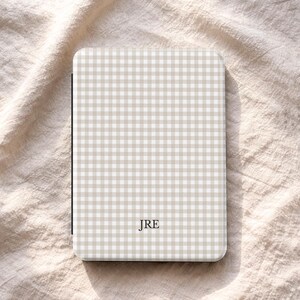 May include: A beige and white gingham pattern case with the initials "JRE" in the centre. The case has a rectangular shape with rounded corners. The brand name "UBLS" is printed at the bottom.
