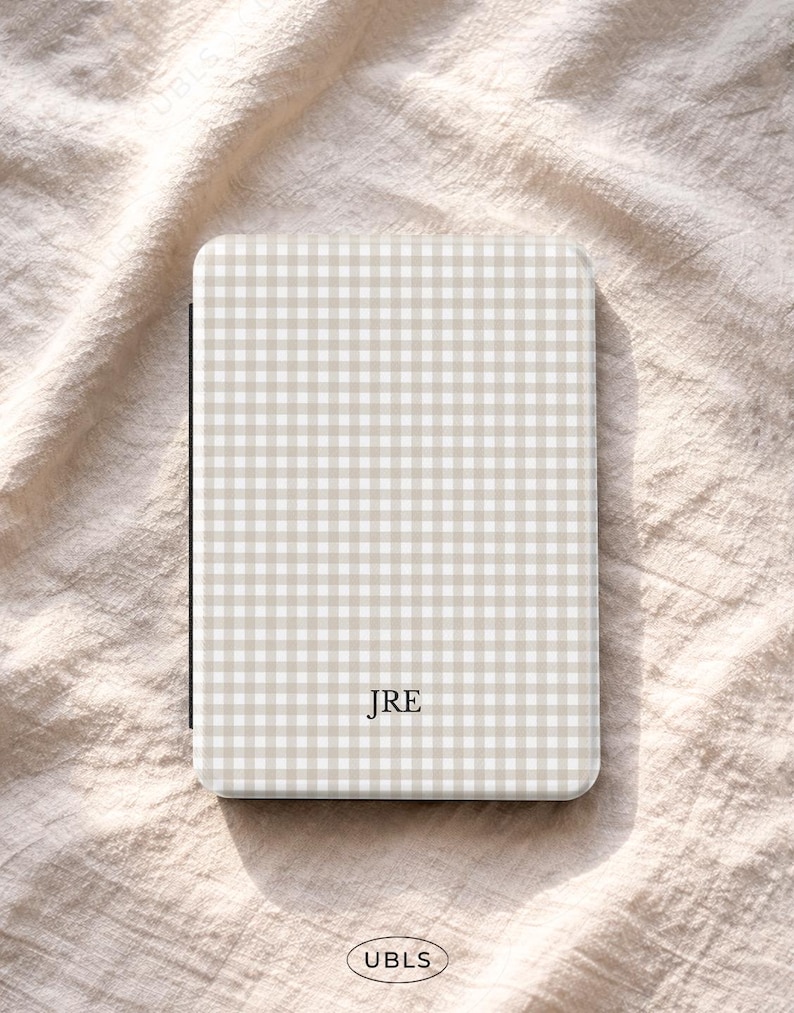 May include: A beige and white gingham pattern case with the initials "JRE" in the centre. The case has a rectangular shape with rounded corners. The brand name "UBLS" is printed at the bottom.
