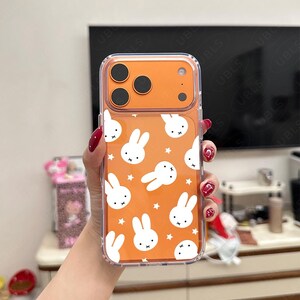 May include: Clear phone case with an orange back featuring a pattern of white bunny faces and stars. The case has a clear border and a camera cutout. The brand name "UBLS" is printed at the bottom.