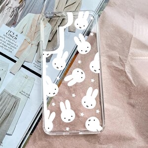 May include: Clear phone case with a white bunny and star pattern. The case has a transparent design, allowing the phone's color to show through. The bunnies have a simple, cartoon-like style.