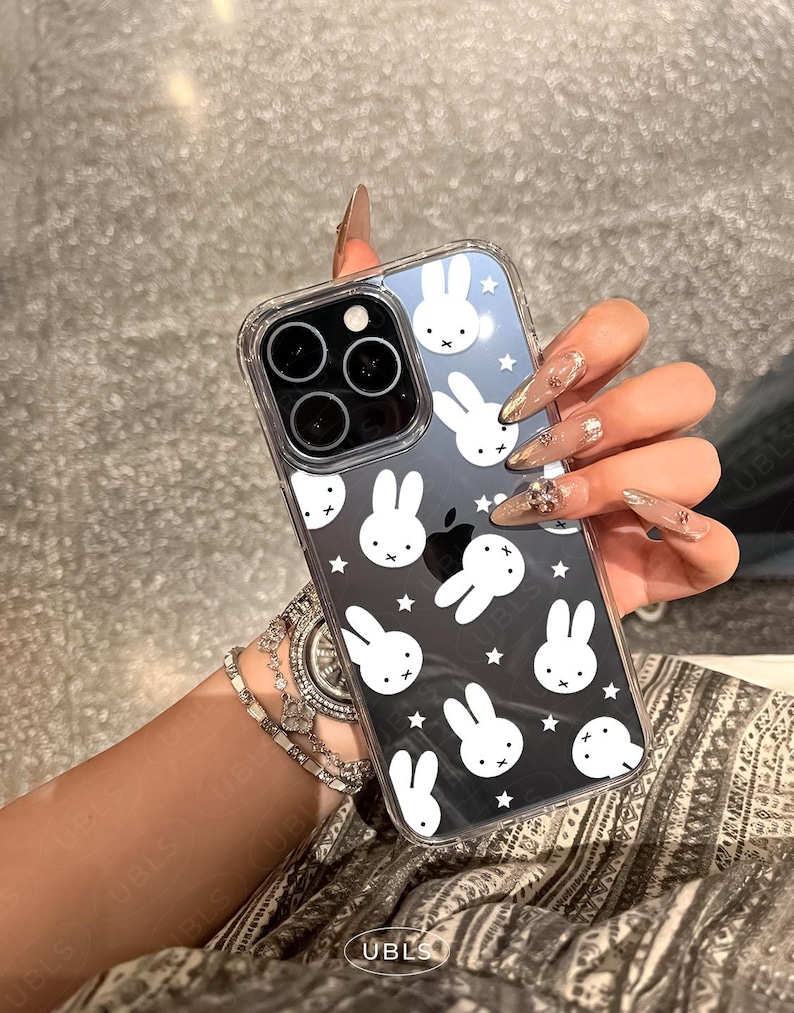 May include: Clear phone case with a black and white bunny pattern. The case has a clear border and covers the back of a smartphone. The design features multiple bunny faces and stars.