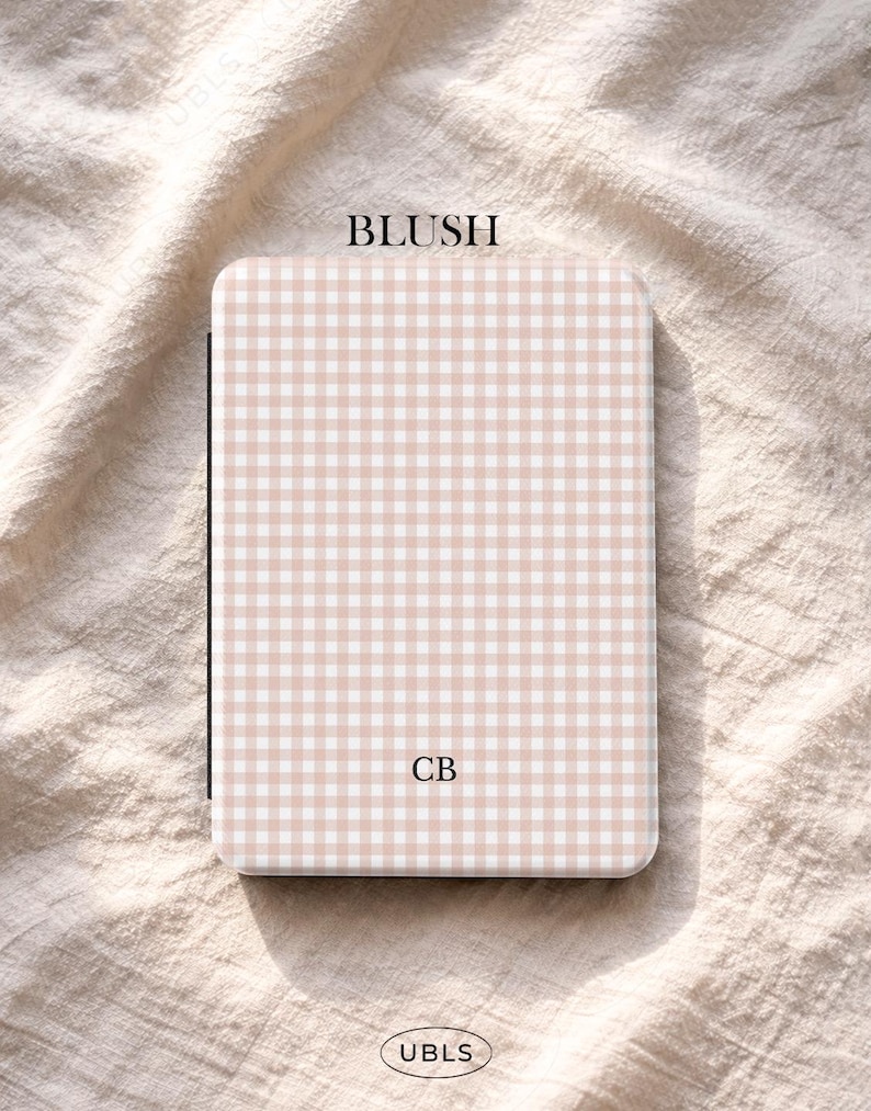 May include: A rectangular case featuring a blush pink and white gingham design. The word "BLUSH" is printed at the top, and the initials "CB" are in the centre. The brand name "UBLS" is at the bottom.