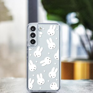 May include: A clear phone case featuring a pattern of white bunny faces and stars on a light gray background. The phone case has a camera cutout and the text "UBLS" at the bottom.
