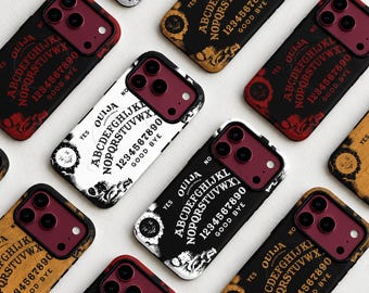 May include: A collection of smartphone cases featuring Ouija board designs with letters, numbers, and the words OUIJA, YES, NO, and GOOD BYE. The cases are available in black, white, and tan colorways, each with a dark red camera lens area.