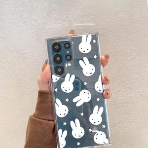 May include: Clear phone case with a repeating pattern of white bunny faces and stars on a dark blue background. The case has a rectangular shape and is designed to fit a smartphone. The brand name "UBLS" is printed at the bottom.