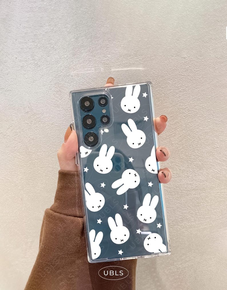 May include: Clear phone case with a repeating pattern of white bunny faces and stars on a dark blue background. The case has a rectangular shape and is designed to fit a smartphone. The brand name "UBLS" is printed at the bottom.