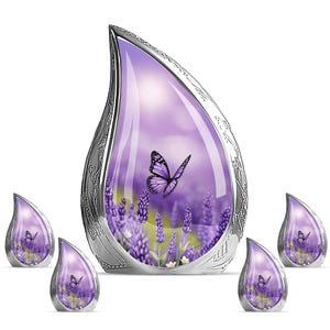 Puede incluir: Urna decorativa plateada en forma de lágrima con un diseño de campo de lavanda y mariposa. La urna tiene un interior púrpura y está rodeada de urnas más pequeñas a juego. La mariposa es púrpura con marcas negras.