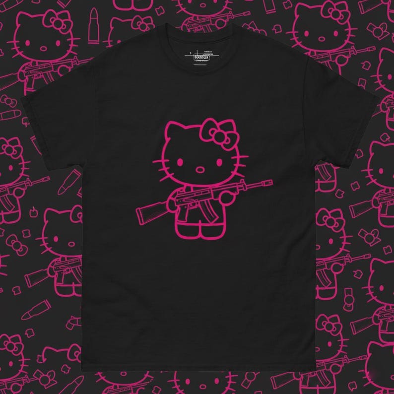 Puede incluir: Camiseta negra con un contorno rosa de un gato de dibujos animados sosteniendo un rifle. El gato tiene un lazo en la cabeza. El fondo tiene un patr&oacute;n repetido del mismo gato, rifle y casquillos.