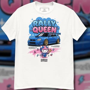 May include: A white t-shirt featuring a graphic of a blue rally car with gold wheels, the text RALLY QUEEN, and a cartoon cat character in a racing suit holding a key. Below the graphic, the text FAST & KAWAII is printed above a barcode.