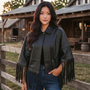 May include: A black jacket with a textured snakeskin pattern, featuring a collared neckline, a single front button closure, and long fringe detailing along the hem and sleeves. The garment is worn over a plain black top and blue denim jeans.