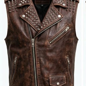 May include: Brown leather vest with silver metal studs and spikes. The vest features a notched collar, a front zipper, multiple zippered pockets, and adjustable buckles at the waist. The vest has a distressed finish.