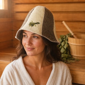 Può includere: Un cappello da sauna in feltro con un design a pannelli in colori alternati crema e marrone scuro. Il pannello frontale presenta un motivo botanico ricamato in verde raffigurante un ramo frondoso. Il cappello ha una tesa larga e arrotondata.