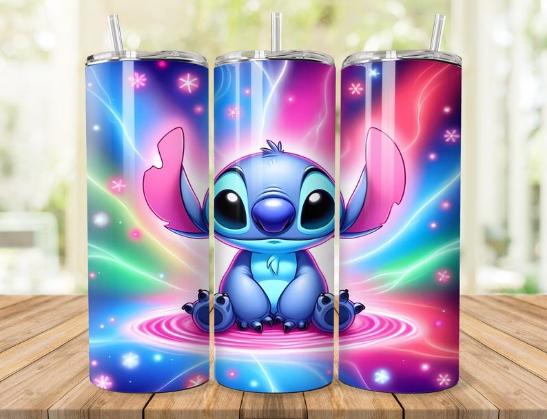 Puede incluir: Juego de tres vasos de acero inoxidable con un dise&ntilde;o de personaje de dibujos animados. El dise&ntilde;o presenta una criatura alien&iacute;gena azul con ojos y orejas grandes, sobre un fondo colorido de tonos rosas, azules y verdes. Cada vaso incluye una pajita.