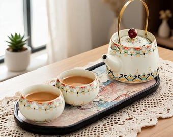 May include: A ceramic tea set featuring a teapot with a gold metal handle and a dark red knob, accompanied by two matching tea cups. The pieces are decorated with a colorful floral pattern and sit on a rectangular black tray with a floral print.
