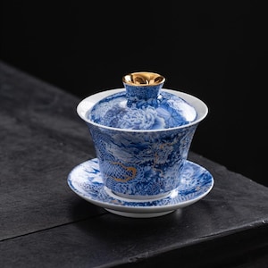 May include: A blue and white porcelain tea set with a matching lid and saucer. The set features a detailed dragon and floral design with gold accents. The tea cup is approximately 3 inches in diameter.