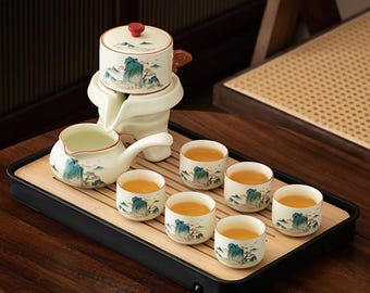 May include: A complete tea set featuring a white ceramic teapot with a red lid, a serving pot, and six small cups. Each piece is decorated with a blue and green mountain landscape design. The set is arranged on a bamboo tray.